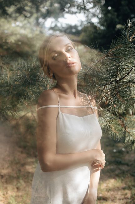 Elegant portrait of a woman in a white dress amidst nature, captured with soft lighting.
