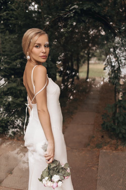 Woman in White Spaghetti Strap White Dress Holding a Bouquet
