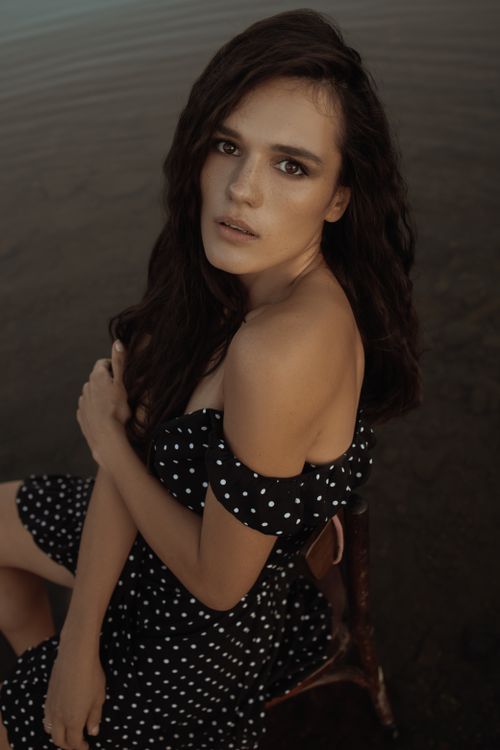 Free A woman with long hair sits outdoors in a polka dot dress, exuding elegance and style. Stock Photo