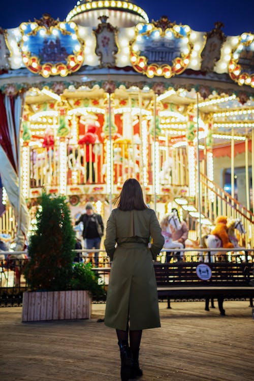 Free Woman Wearing Long Coat Standing in Front of a Carousel Stock Photo