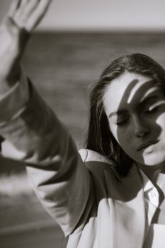 A woman on the beach with eyes closed, casting a shadow on her face with her hand.