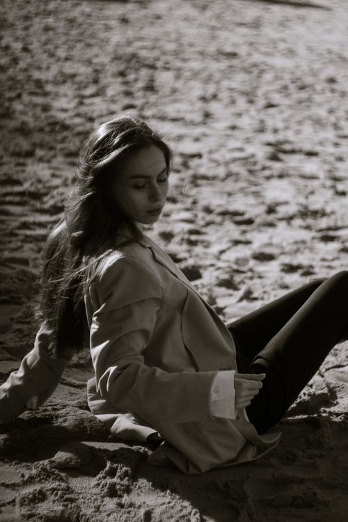 Free Black and white portrait of a woman with long hair sitting on the sand, evoking tranquility. Stock Photo