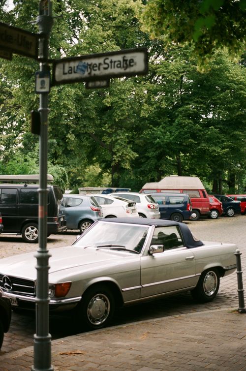 Free A classic Mercedes car parked on a European street with a backdrop of lush trees. Stock Photo