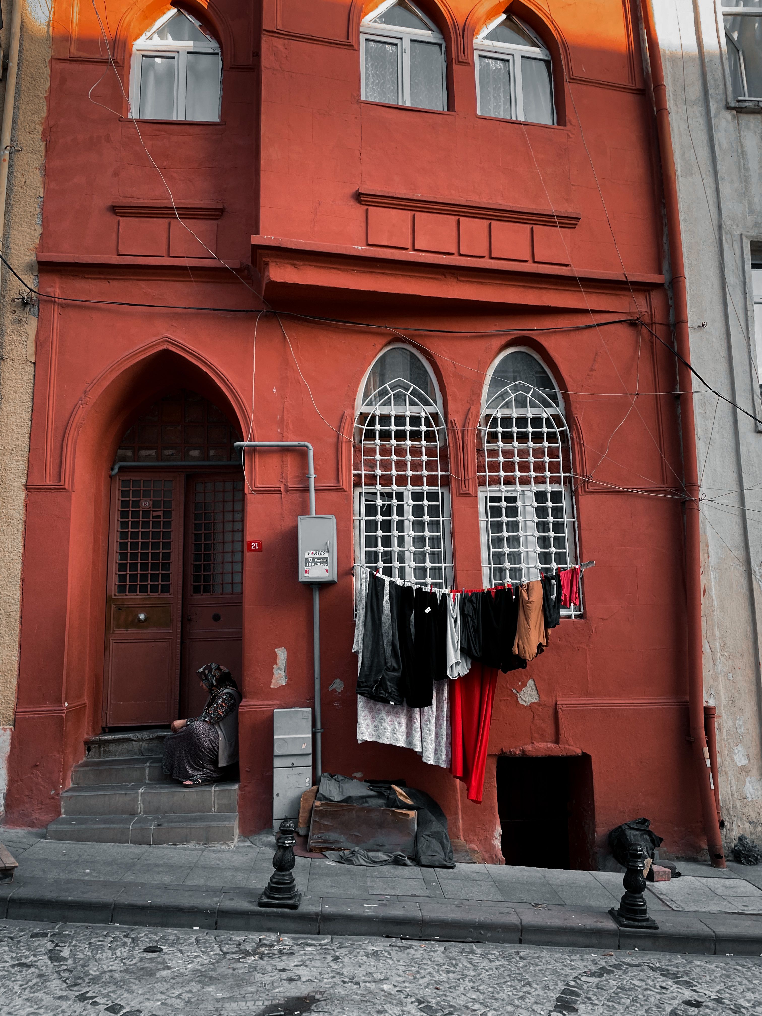 Vertical shot of a red building with laundry hung outside and a person sitting on steps.