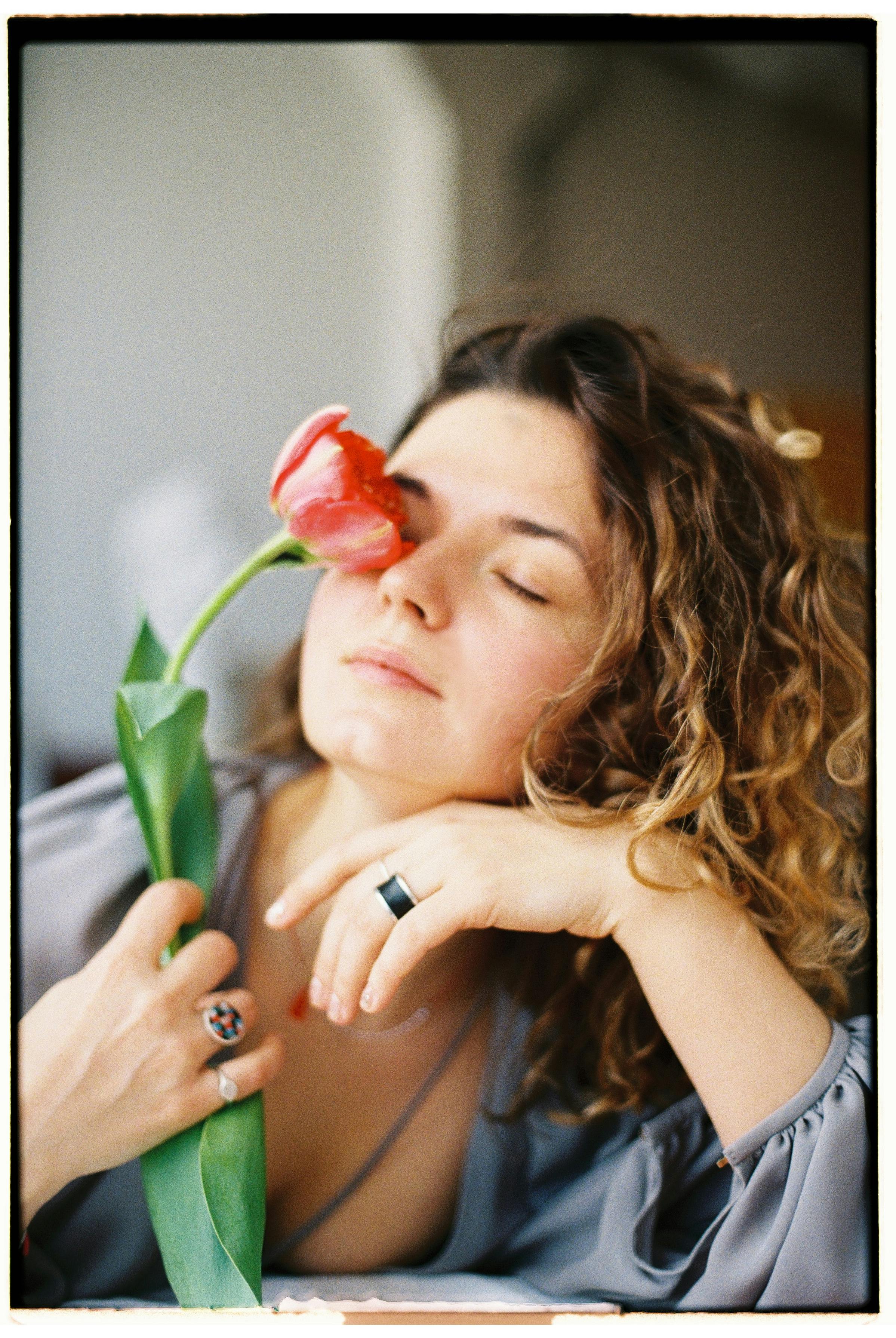 Serene woman holding a red tulip with eyes closed, evoking calmness.