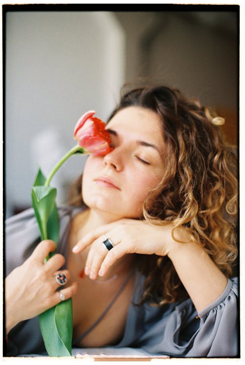 Young woman holding rose flower close to eyes