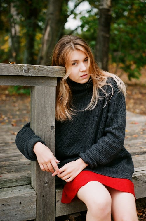 Young blond woman sitting near wooden barrier in autumn