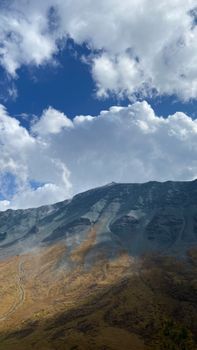 A stunning view of a towering mountain peak against a backdrop of blue skies and white clouds.