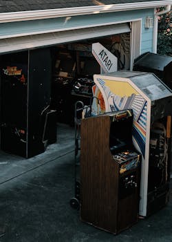 A collection of vintage arcade machines stored in an open garage, showcasing retro gaming history.