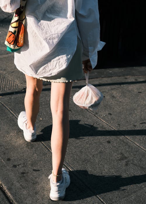 A Woman in White Long Sleeves Walking on Gray Concrete Pavement