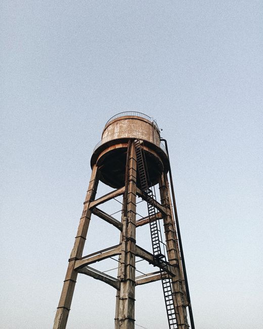 An old rustic water tower made of metal against a clear blue sky viewed from below.