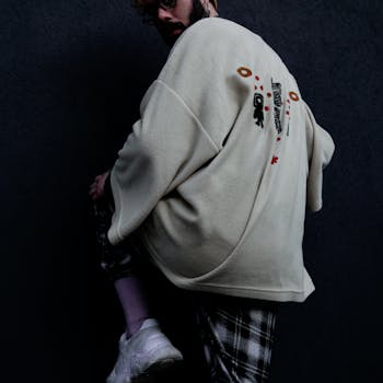 Fashionable man in an oversized sweater posing with urban dark backdrop and white sneakers.