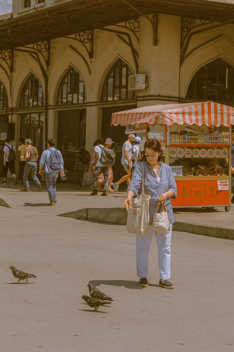 A Woman Feeding Birds On The Street