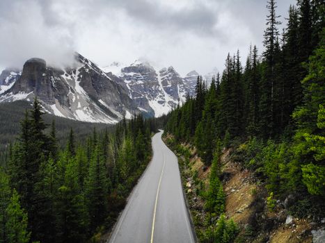 A winding road through Banff National Park with snow-capped mountains and dense forests.