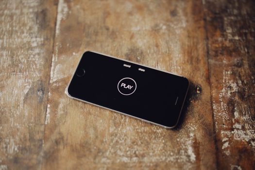 Close-up of a smartphone on a wooden table showing a play icon on its screen.