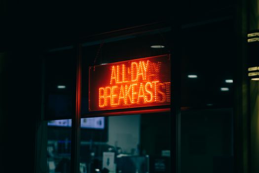 Bright red neon sign advertising all-day breakfast in a window at night.