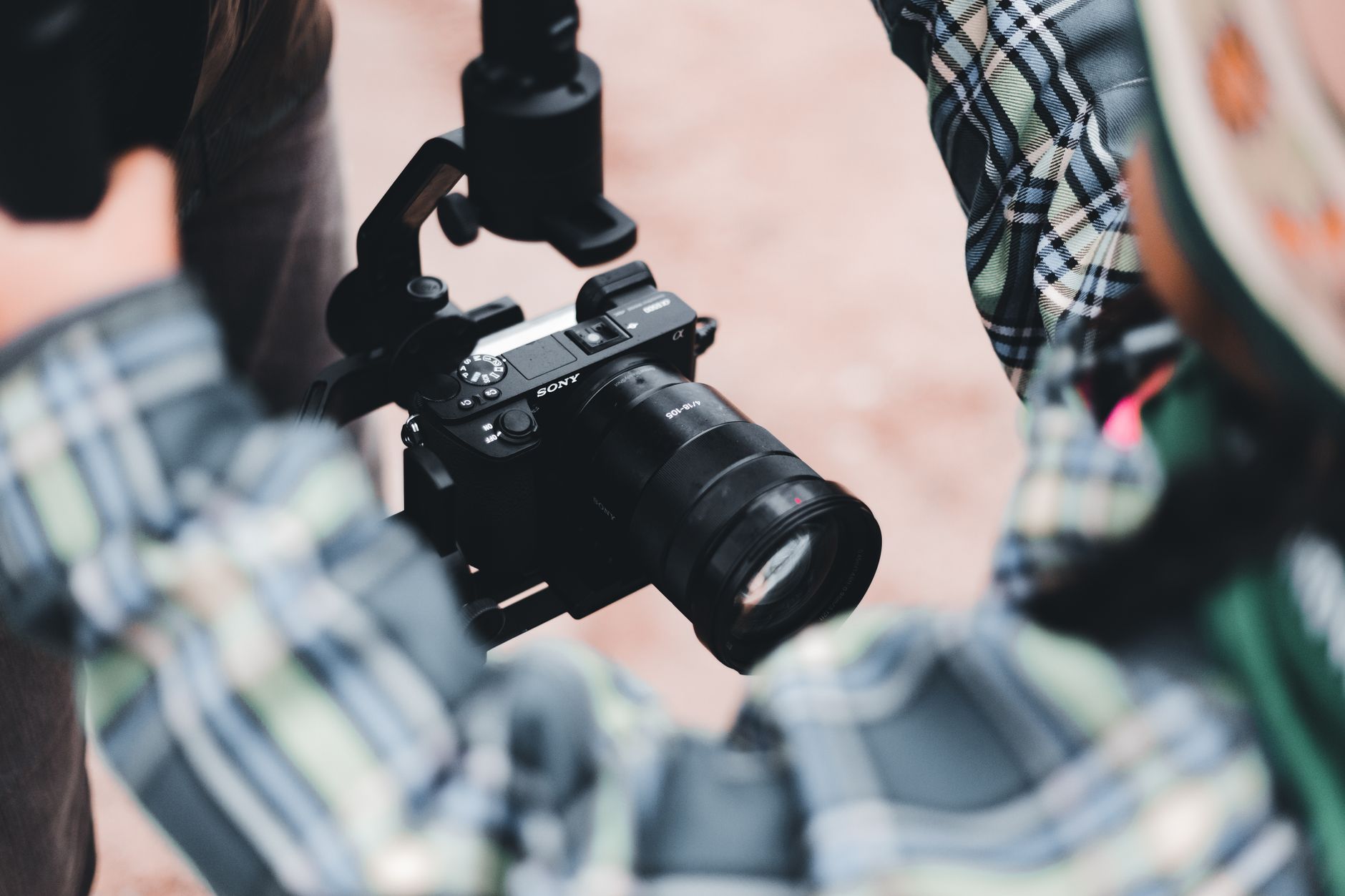 Outdoor shot focusing on a camera mounted on a stabilizer, held by a person in plaid clothing.