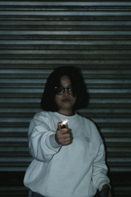 Free A woman in a white sweatshirt holds a lit lighter in front of a metal shutter. Stock Photo