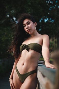 A confident woman poses in a green bikini, showcasing style and elegance outdoors.