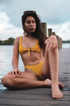 Woman in yellow bikini sitting on a dock by the water. Moody beach day.