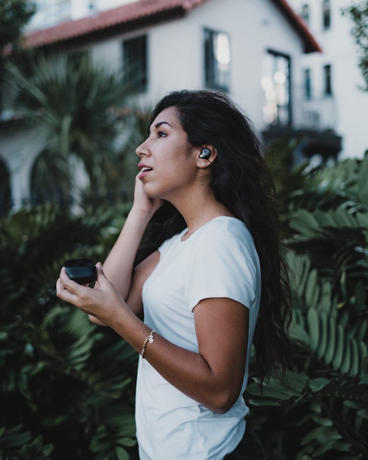 A Woman In A White Shirt Using Wireless Earbuds