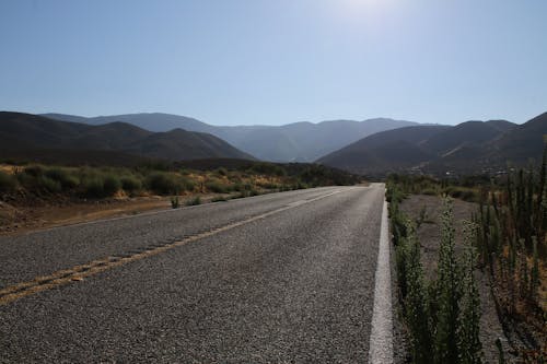 Gray Concrete Road Between Green Grass Field and Mountains