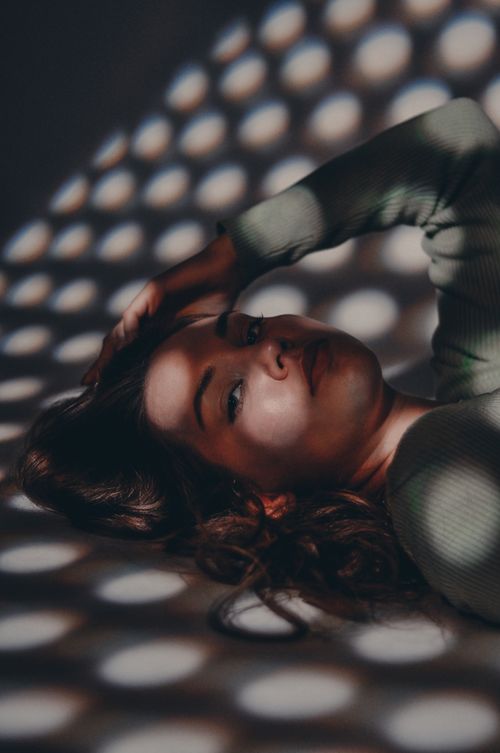 Free A woman lies under artistic light patterns creating an intriguing shadow effect. Stock Photo