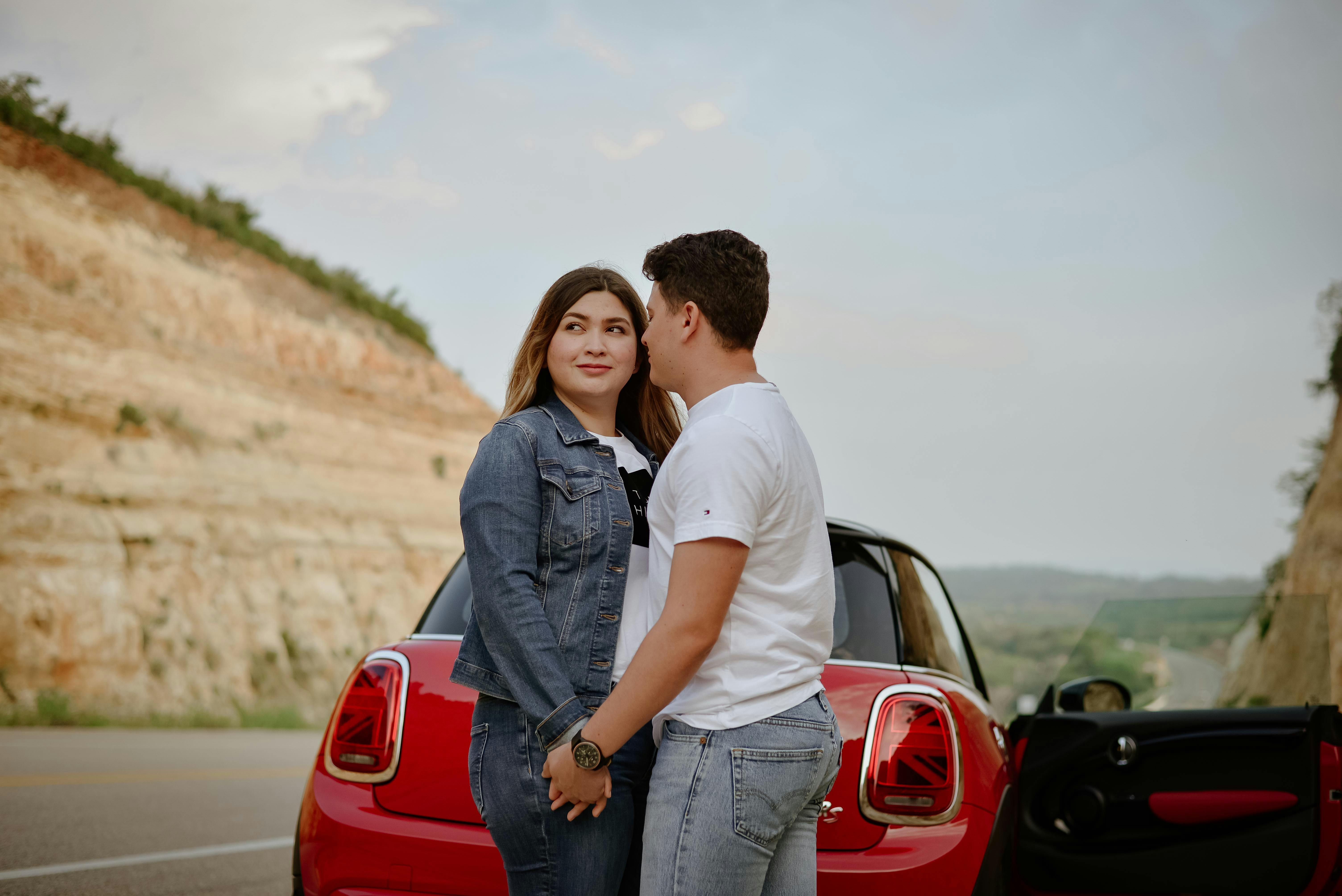 partnership opportunities for US travel agencies mexico - A couple stands by a red car on a scenic road, symbolizing love and adventure.