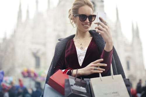栗色的長袖上衣，白天拿著智能手機與購物袋的女人