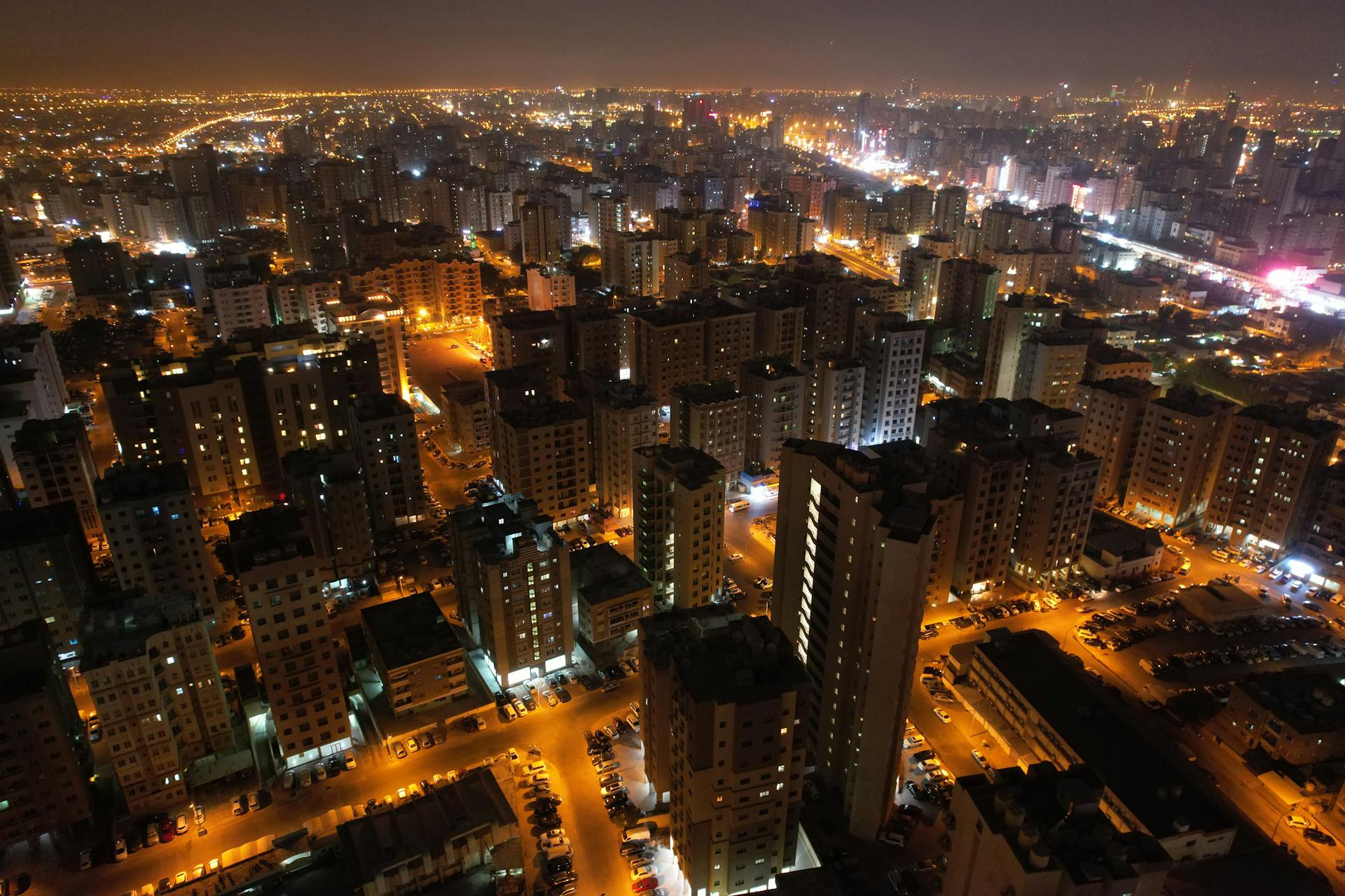 Drone shot of illuminated skyscrapers in Kuwait City under the night sky.