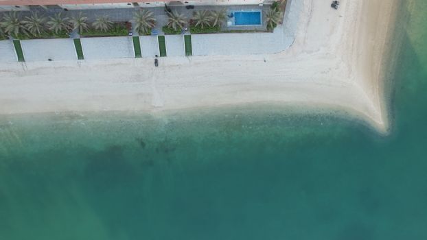 A top-down aerial shot of a sandy beach and palm trees by the turquoise sea in Kuwait.