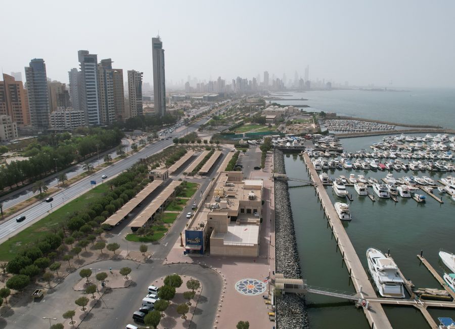 Aerial view of Kuwait City's modern skyline and bustling harbor with yachts.