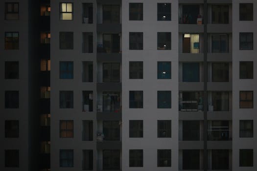 A detailed view of a modern apartment building facade with illuminated windows at night.