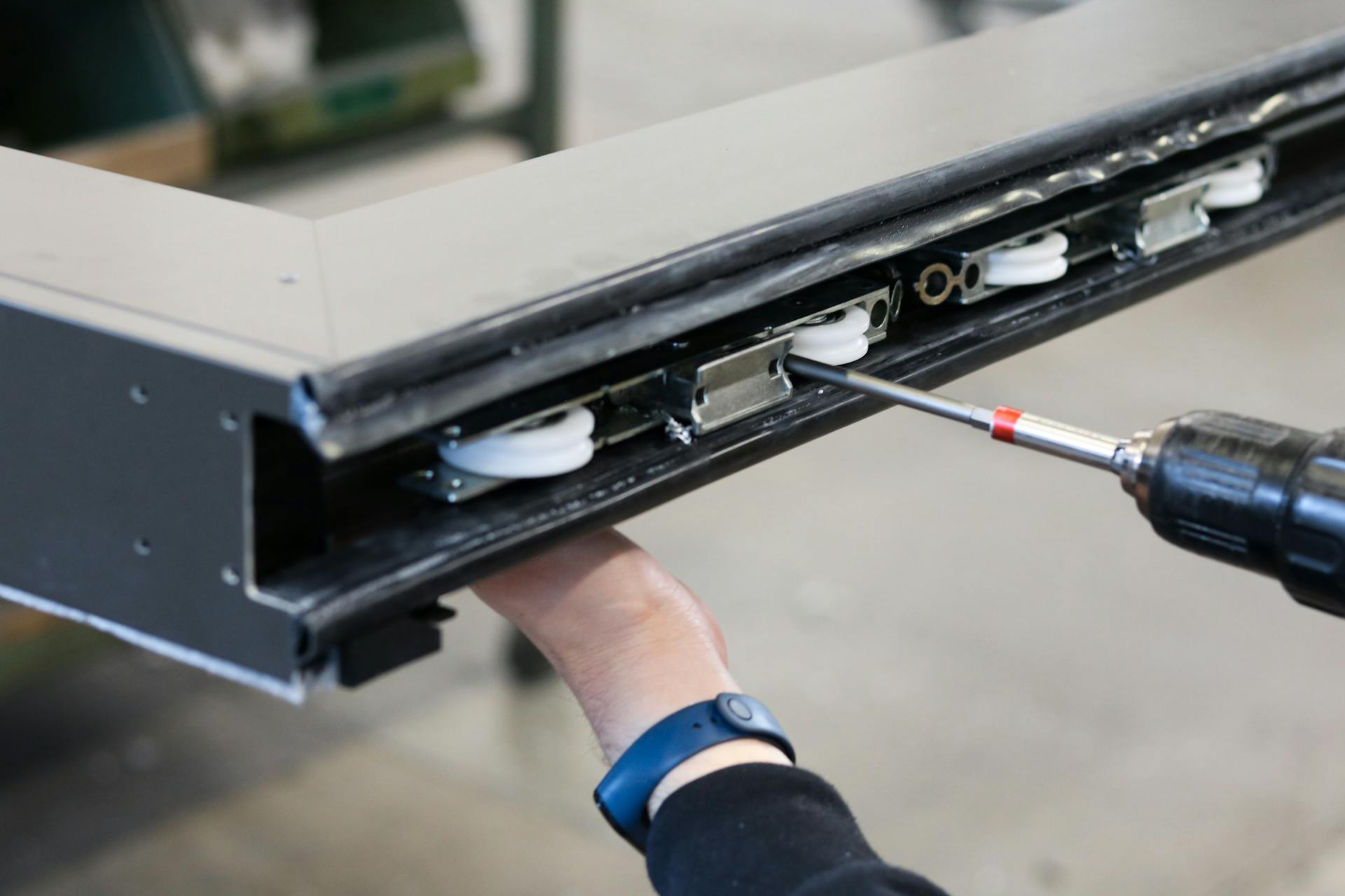 Close-up of a worker using a drill to assemble metal components indoors.