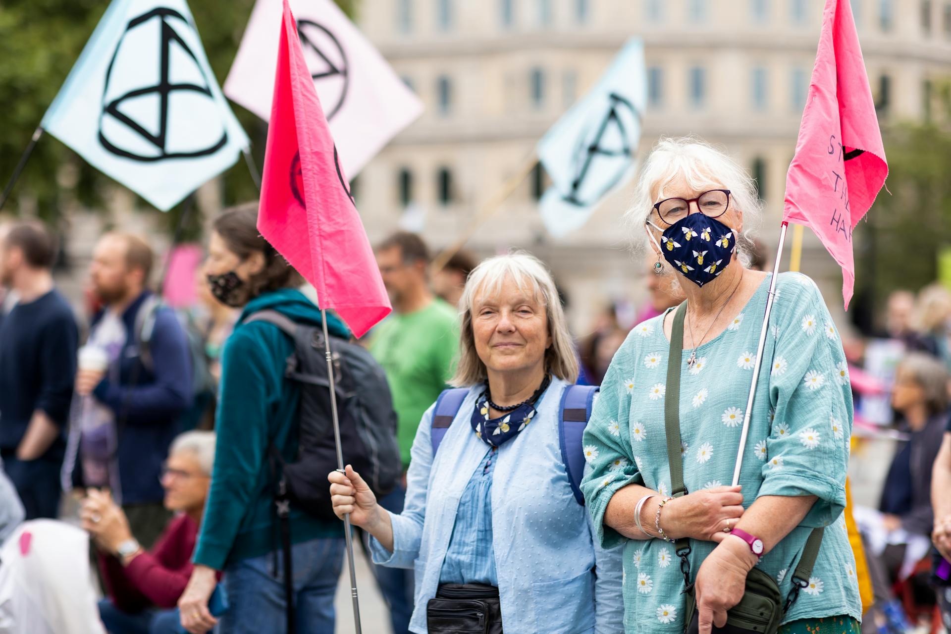 Two elderly women with flags and masks at a street protest advocating for climate change action.