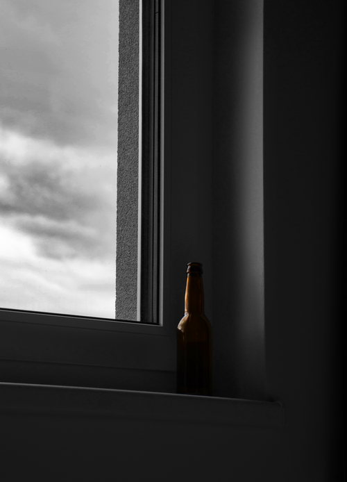 Free A solitary beer bottle rests on a windowsill against a moody sky backdrop. Stock Photo