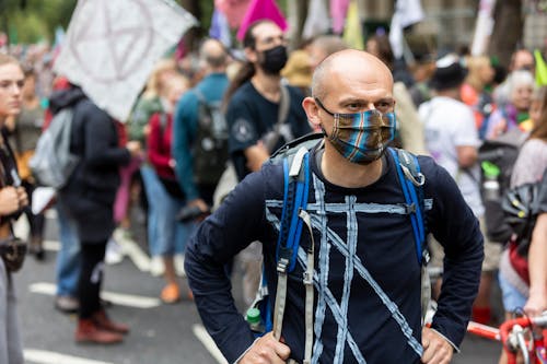Concentrated adult male in mask and with backpack standing in street near crowd of protesters