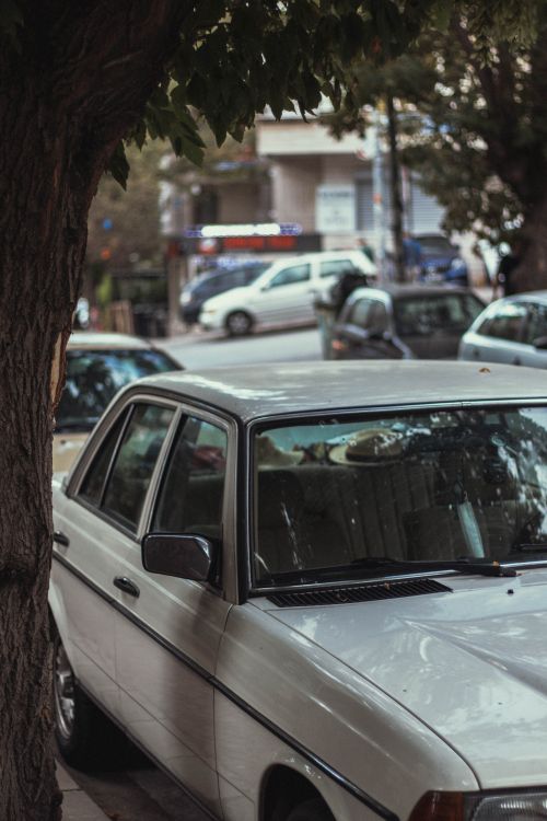 Free A timeless vintage car parked by a tree on a bustling urban street during the day. Stock Photo