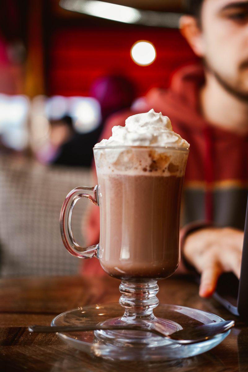 Ciocolată caldă cu frișcă servită într-un pahar, într-o cafenea