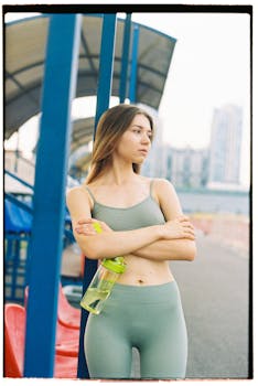 Caucasian woman in athletic wear standing by a track with arms crossed, looking away.