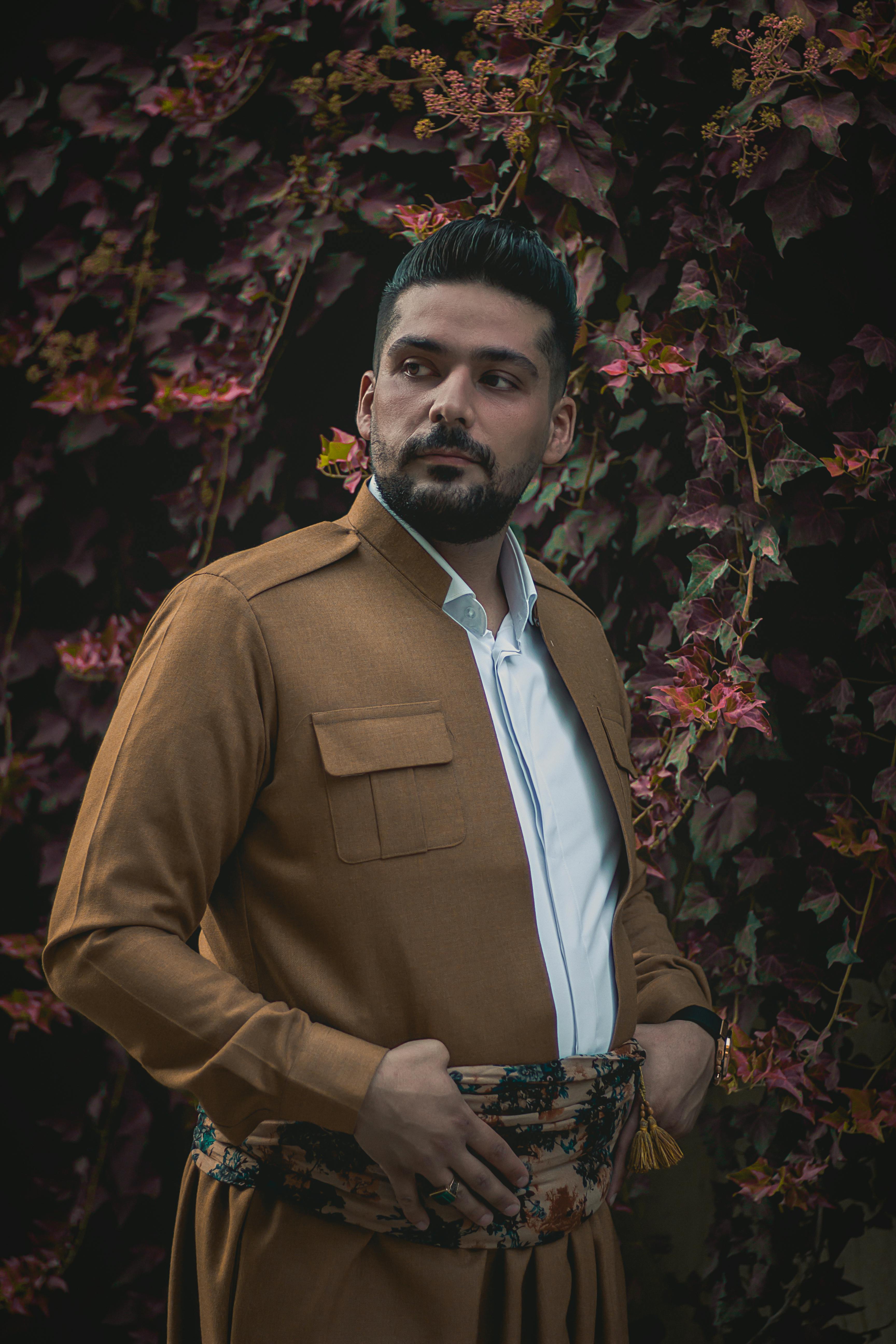 Man in traditional Kurdish attire posing outdoors against an autumnal backdrop.