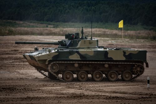 Free A camouflaged tank driving through a muddy field with trees in the background. Stock Photo