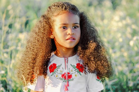 Charming portrait of a young girl with curly hair and a floral top, standing outdoors in natural light.