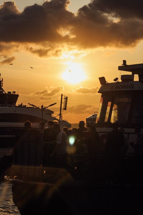 Free Sunset view of a ferry with silhouetted passengers and birds in the harbor. Stock Photo