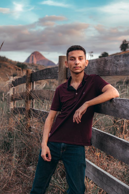 A Man Wearing a Polo Shirt Leaning on a Wooden Fence