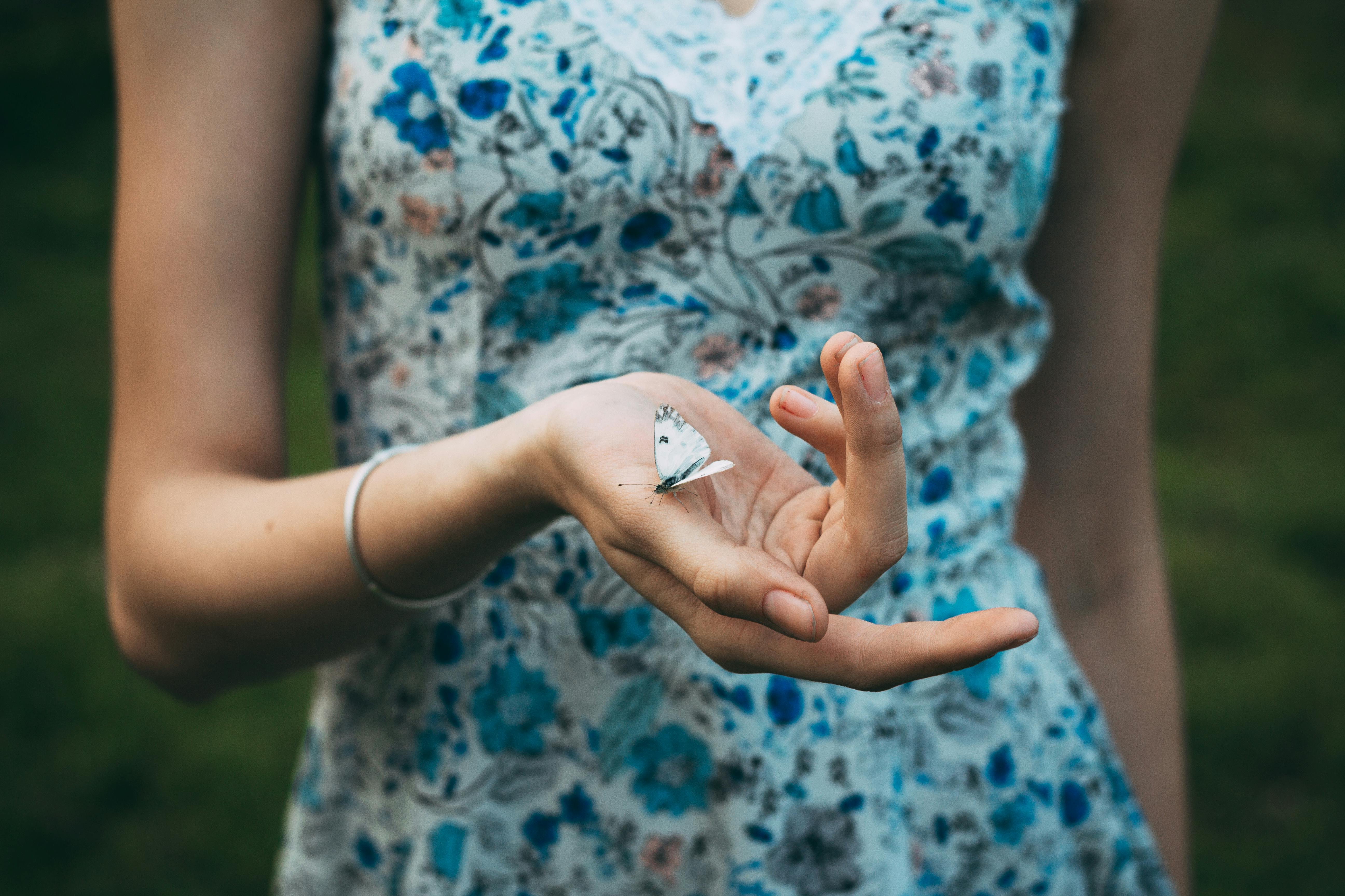 Close-up of a woman gently holding a butterfly outdoors.
