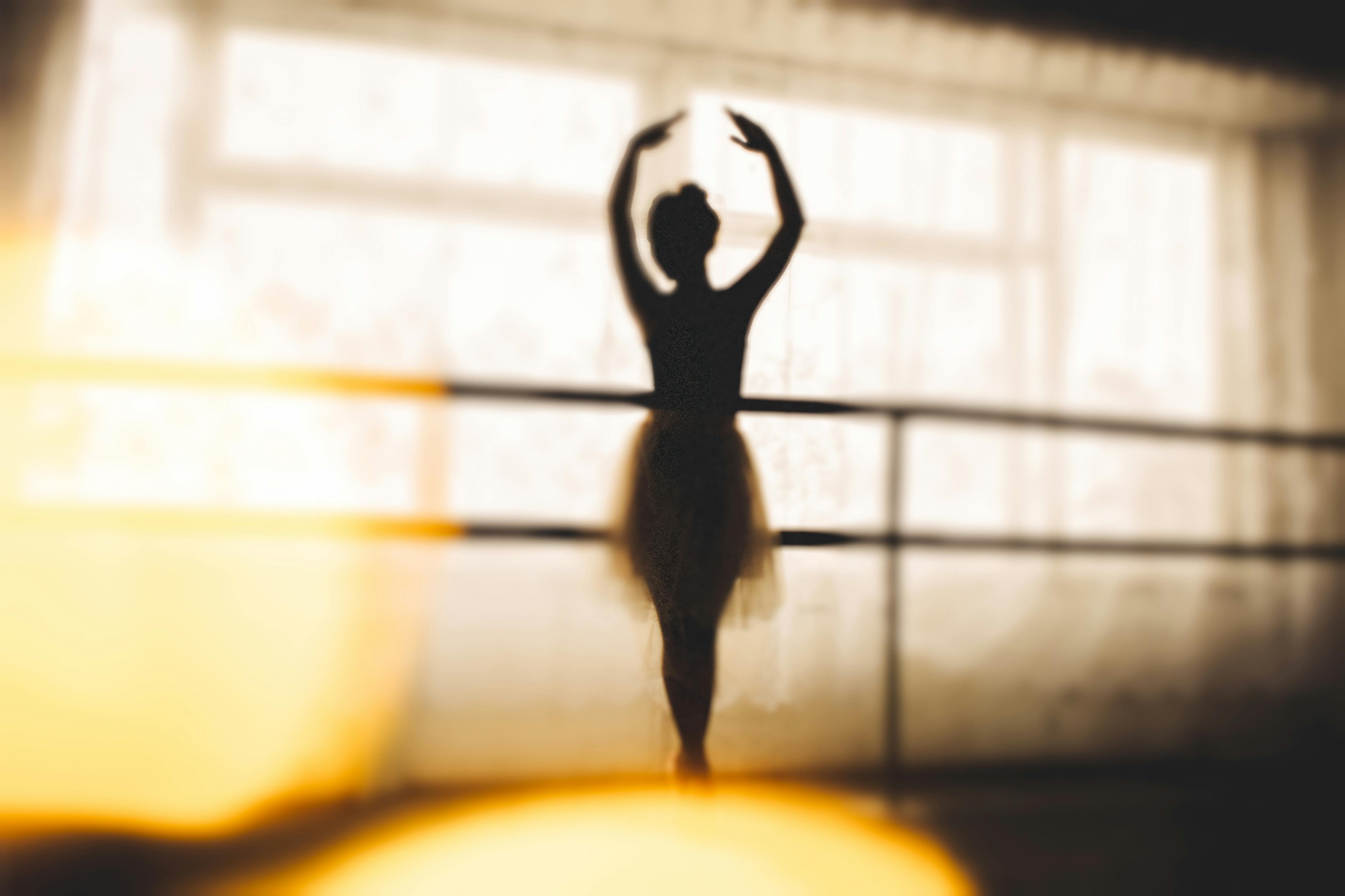 Elegant silhouette of a ballerina posing gracefully in a sunlit dance studio.