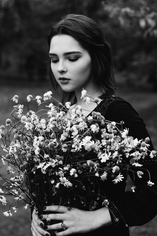Grayscale Photo of a Woman Holding a Bunch Flowers