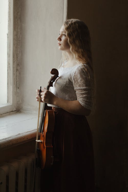 Blond girl standing next to window with violin in hand