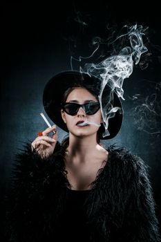Portrait of a stylish woman in a fur coat and hat smoking in a moody studio setting.